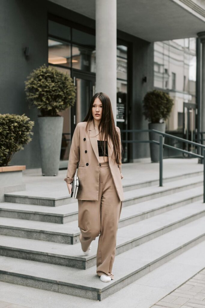 Modern tailored style featuring a double-breasted beige blazer and matching wide-leg trousers on a woman walking down stone steps.