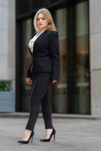 A woman wearing a black blazer and tailored charcoal jeans with black heels.