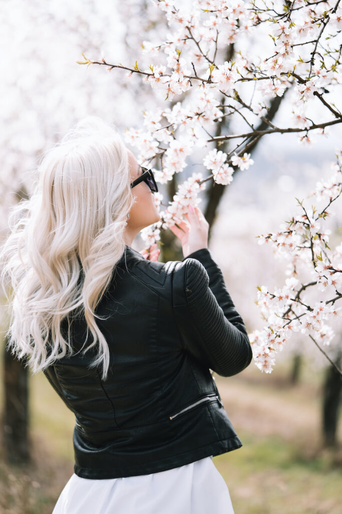 Luxury casual outfits featuring a cropped black leather jacket paired over a flowing white dress in a spring blossom setting.