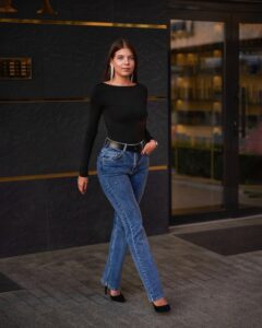 A woman walking wearing a black top, blue slim-fit denim jeans and black high heels.