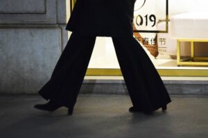 A person walking wearing black wide-leg trousers and black heels.