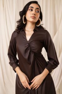 A woman wearing a chocolate brown silk dress with ruching detail and large silver hoop earrings.