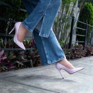A woman wearing denim jeans with a high-slit in the hem and soft pink stiletto heels.