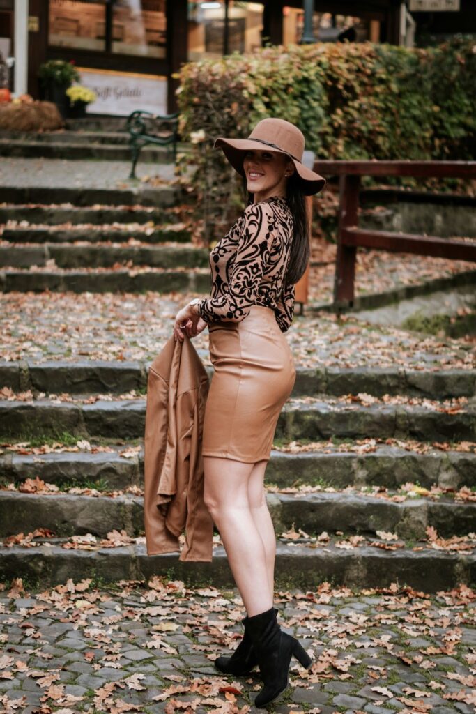 Luxury casual outfit showcasing a monochrome tan leather skirt and matching jacket with a wide-brimmed hat in an autumn setting.