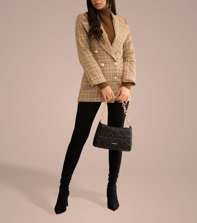 As part of the capsule wardrobe essentials edit, a woman holding a black bag, wearing a plaid blazer, black leggings and black ankle boots.