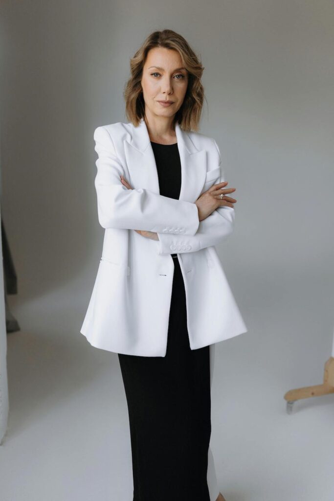 For our Capsule Wardrobe Essentials Edit we have a woman standing with arms crossed wearing a white blazer over a maxi black dress. 