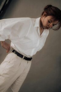 A woman wearing a white blouse tucked into light cream trousers and a black belt.