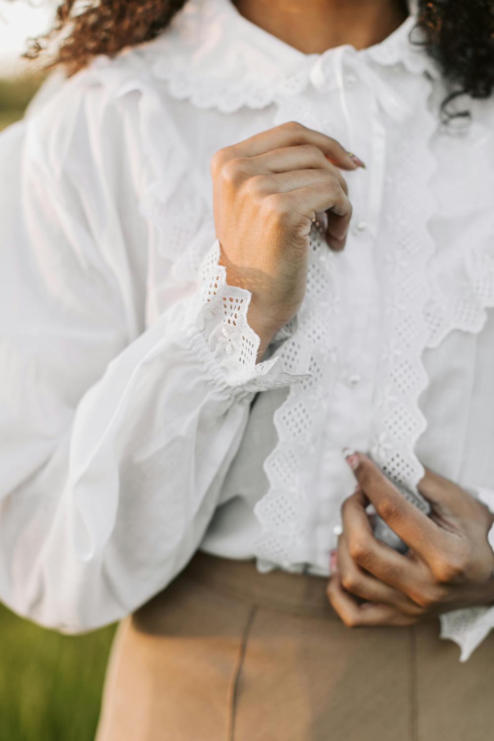 For the capsule wardrobe essentials edit, we have a close-up of a white high-neck blouse with ruffled lace trim and button-down front paired with tan trousers.