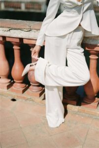 A woman wearing a white suit adjusting her white high heel shoe.
