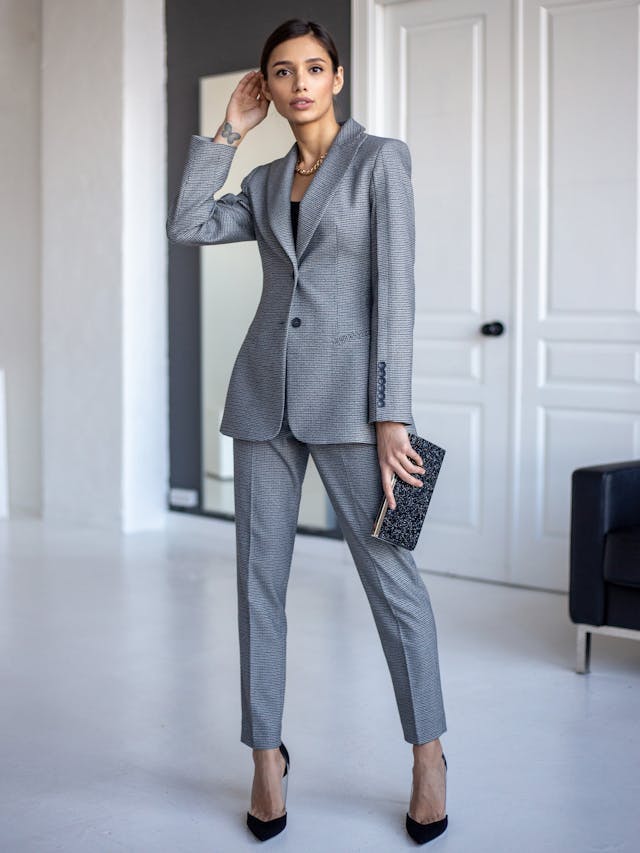 Woman wearing a tailored grey houndstooth blazer and matching trousers for a modern blazer edit.