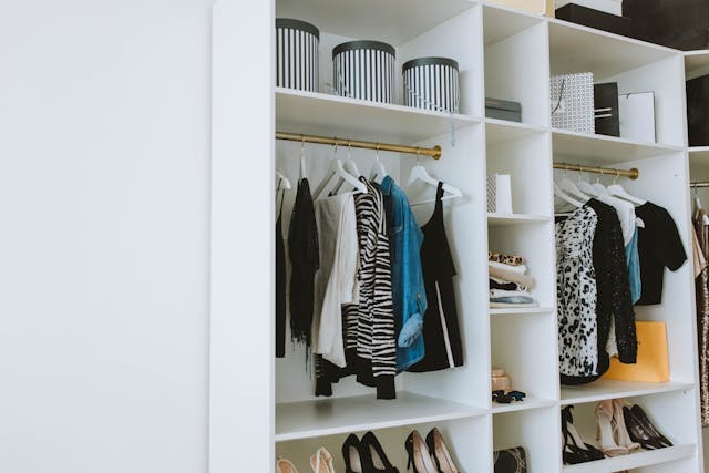 A modern and organised white walk-in closet with structured clothing, striped storage boxes, and shoes neatly arranged on shelves.