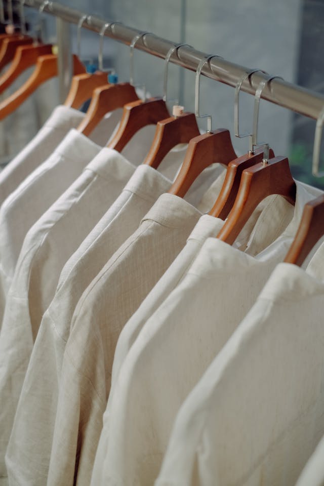 A close-up shot of minimalist white shirts hanging neatly on structured wooden hangers on a clothing rack.