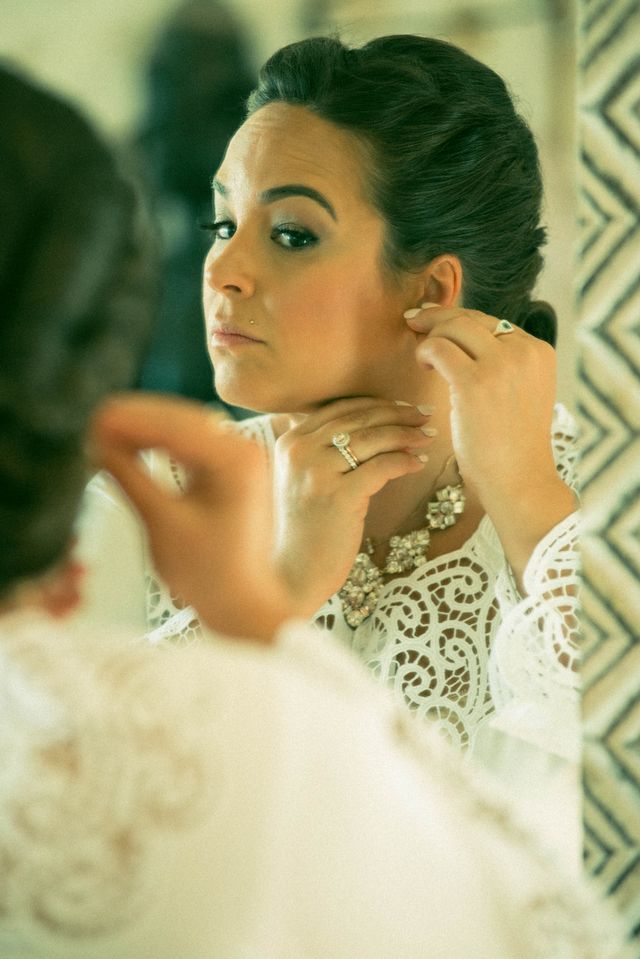 Intimate mirror reflection of a serene woman looking at her reflection while adjusting her earring, capturing a mindful morning routine and quiet self-confidence. 
