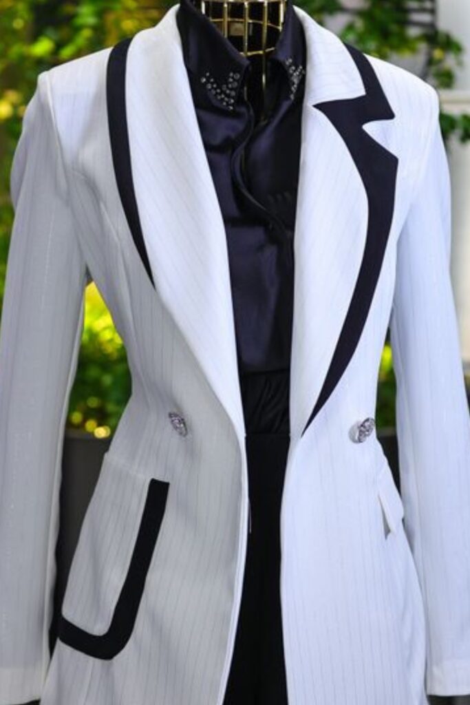Tailored white blazer with black contrast lapels layered over a dark silk button-up blouse with subtle collar embellishments on a mannequin. 